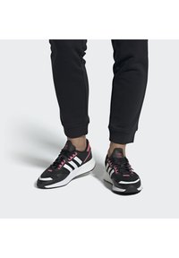 Zapatillas deportivas negras con franjas blancas y acentos rosas, con parte superior de malla, suela acolchada y diseño de punta redondeada.