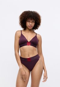 Set de lenjerie intimă burgundy de la Calvin Klein, ce include un bralet triangular și o pereche de chiloți cu tăietură înaltă, ambele având un braț cu logo. 