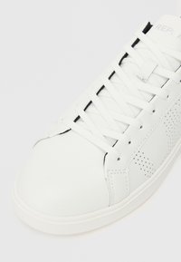 Witte synthetische leren sneaker met platte veters, ronde neus, geperforeerd zijontwerp en een textuurzool voor grip. Minimalistische stijl.