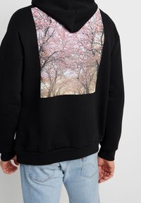 Felpa nera con cappuccio caratterizzata da una grande grafica di alberi di ciliegio in tonalità di rosa sul retro, con polsini e orlo a coste.
