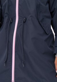 Marinblå vindjacka med dragkedja framtill, prydd med rosa och vita ränder, justerbara dragsnöre och sidofickor med flikar.