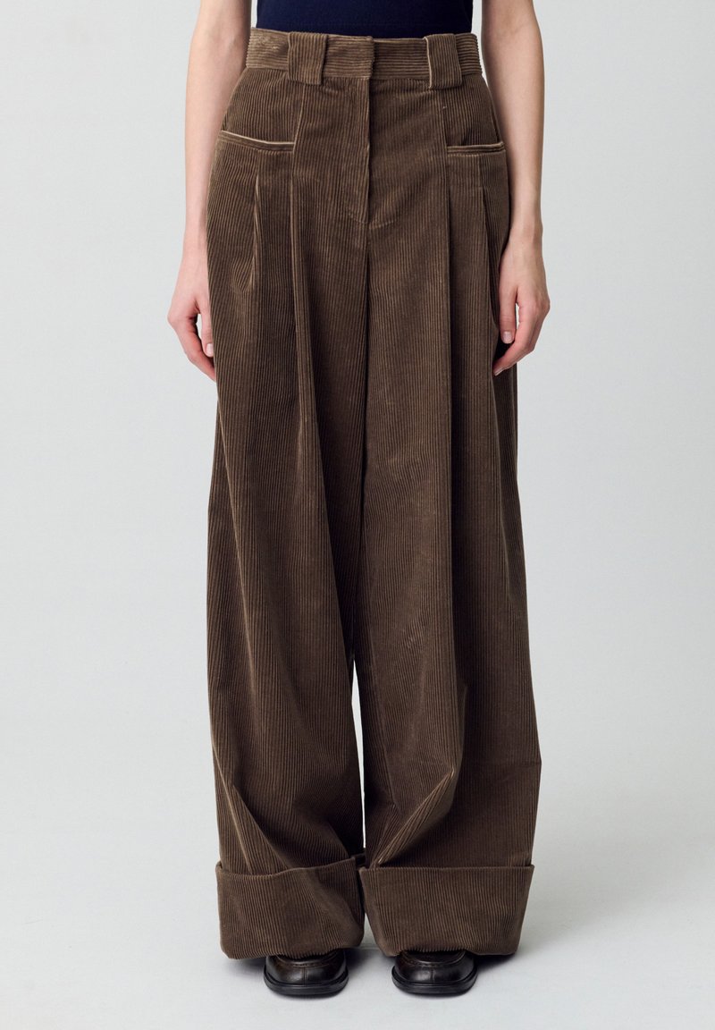 Pantaloni a gamba larga in corduroy marrone con profonde pince frontali, due tasche laterali e risvolti; tessuto testurizzato con righe verticali.