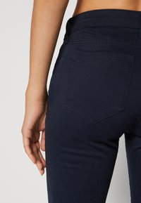 Námornícke modré džínsy vyrobené z bavlny, so slim fit strihom, detailmi na zadných vreckách a jednoduchým pásom. Viditeľná textúrovaná tkanina.