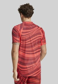 Jersey corto de manga corta rojo con patrones ondulados y punteados. Hecho de material ligero con una textura suave. Acentuado con costuras contrastantes.