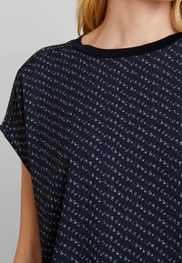 Mörkblå t-shirt med korta ärmar, prydd med ett litet blomster mönster i vitt och rosa, samt en enfärgad svart halsringning. Mjukt tyg.