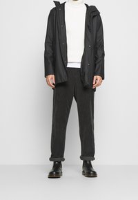 Schwarze wasserdichte Jacke mit Kapuze, kombiniert mit einem weißen gerippten Rollkragenpullover und grauen Cordhosen, vervollständigt mit schwarzen Lederstiefeln.