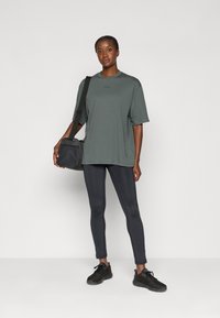 Prevelký šedý tričko v kombinácii s čiernymi legínami. Model má malú crossbody kabelku. Hladká tkanina s voľným strihom. Čierne tenisky.