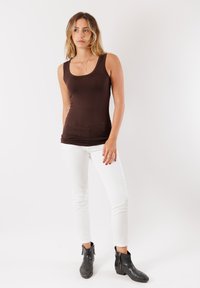 Top tank color marrone abbinato a jeans slim-fit bianchi e stivaletti neri alla caviglia. Il top ha un collo a barca e una vestibilità aderente.