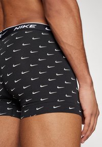 Schwarze Boxer-Shorts mit einem wiederholten weißen Nike-Swoosh-Muster, ausgestattet mit einem kontrastierenden weißen Bund, der das Nike-Logo trägt.