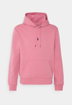 Růžová mikina s kapucí, přední kapsou na kangaroo, nastavitelnou šňůrkou na kapuci a malým námořnicky modrým logem Polo Ralph Lauren uprostřed hrudi.