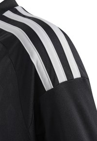 Maillot de sport noir avec trois rayures blanches horizontales sur l'épaule. Fabriqué en tissu texturé avec un détail de couture distinct.
