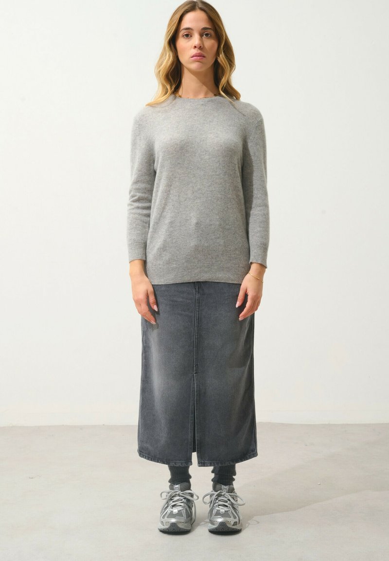 Maglione grigio a maglia con maniche lunghe, abbinato a una gonna maxi in denim scuro con uno spacco frontale. Indossato con sneakers grigie e calzini.