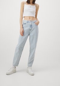 Ljust blå högmidjade jeans med lös passform och uppvikta anklar, tillsammans med en vit kortärmad topp med en liten logotyp. Vita sneakers.