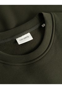 Olivgrüner Pullover mit geripptem Rundhalsausschnitt und einem Etikett mit der Aufschrift "LES DEUX." Weiche Textur, mittelschwerer Stoff und lockere Passform.