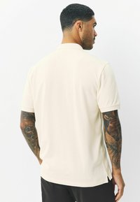 Heren polo met korte mouwen in licht crémekleur, voorzien van een zachte stof, geribde kraag, zijsplitten en subtiele stikdetails.
