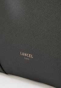 Fekete texturált bőr táska sima felülettel, aranyozott "LANCEL PARIS" logóval az elején. Kompakt és téglalap alakú dizájn.