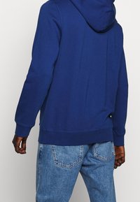 Felpa blu navy con tasca a marsupio, polsini e orlo a costine. Realizzata in morbido cotone, con cappuccio regolabile e design della schiena senza cuciture.