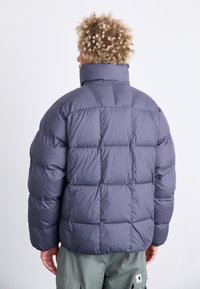 Giacca a vento in grigio scuro con design trapuntato e colletto alto. Presenta una texture liscia e polsini elasticizzati, adatta per il clima freddo.