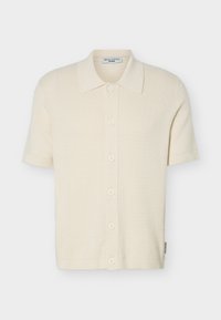 Κρεμ πλεκτή ζακέτα με κοντά μανίκια, διακοσμητικό υφή, κουμπιά μπροστά και κλασικό γιακά, σε απλό φόντο.