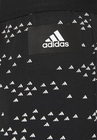 Czarna sportowa tkanina z powtarzającym się białym trójkątnym wzorem, z czarną metką z logo adidas w górnej części.