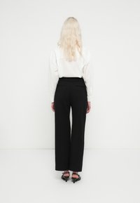 Pantalones anchos negros de talle alto, acompañados de una camisa blanca de manga larga, vistos desde atrás. Tejido liso; sin patrones visibles.