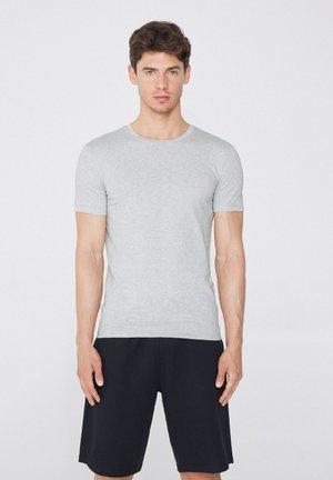 T-shirt gris à manches courtes en tissu doux, avec un col rond. Porté avec un short noir, mettant en avant un design simple et une coupe confortable.