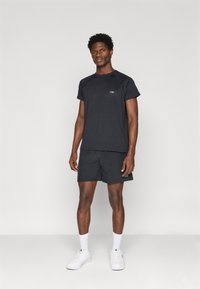 Melnās sporta t-kreklis un šorti, kas izgatavoti no viegla auduma. Iespējas: īsas piedurknes, minimāls zīmola tēls un kontrastējoša balta apavi.