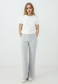 Weißes T-Shirt mit kurzen Ärmeln, kombiniert mit hellgrauen weit geschnittenen Sweatpants mit Seitentaschen und kontrastierenden Nahtdetails. Weiße Sneakers runden das Outfit ab.