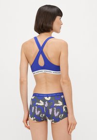 Σπορ στηθόδεσμος σε μωβ απόχρω�ση με σταυρωτές τιράντες και λευκή ελαστική ζώνη. Βερμούδα με σχέδια και αφηρημένα σχέδια σε μπλε, λευκό και γκρι.