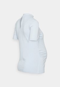 Top de maternidade em azul claro, com relevo, mangas curtas, gola alta e drapeado lateral para um ajuste justo. Detalhe de abertura nas costas.