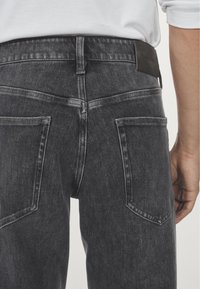 Jeans in denim grigio scuro con design aderente, caratterizzati da una trama liscia, cuciture visibili, due tasche posteriori e un'etichetta in pelle sulla vita.