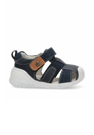 Sandalia azul marino con acentos de denim, correa de velcro, diseño de punta abierta, suela de goma texturizada blanca y detalles de costura en contraste.