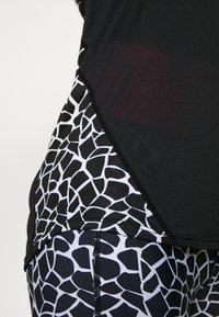 Černobílé sportovní tričko a legíny s texturovaným zvířecím vzorem na legínách a jednobarevnou černou horní částí s viditelnými švy.