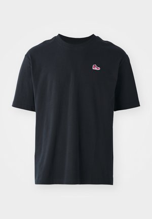 Czarna bawełniana koszulka z krótkim rękawem, okrągłym dekoltem i małym czerwonym logo trampka wyszytym na lewej piersi. Gładka tekstura i minimalistyczny design.