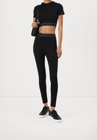 T-shirt noir court et leggings taille haute avec une ceinture logo contrastante, associés à des baskets noires avec une semelle blanche.