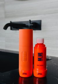 Twee feloranje body sprays. Een hoge met ribbelstructuur, gelabeld "WARM-UP BODY SPRAY," en een kortere, ronde met een roze dop.