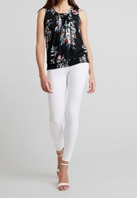 Floral-patterned sleeveless black blouse with pleats, paired with white skinny jeans and white strappy heels. Smooth fabric, relaxed fit.