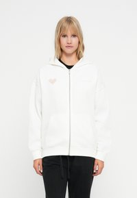 Hvit zip-up hettegenser med en stor lomme, har et rosa hjerte-logo på venstre bryst, laget av myk stoff med en avslappet passform.