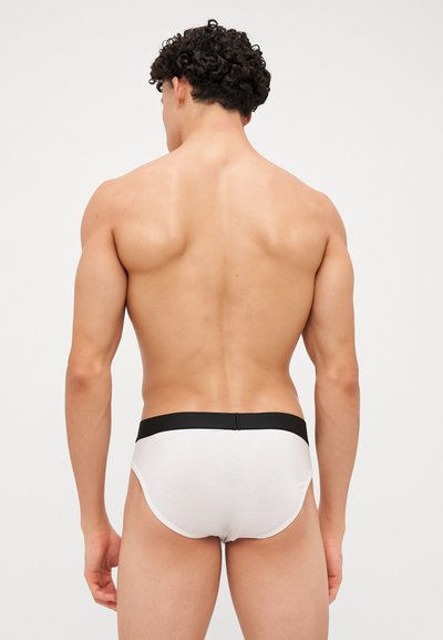 Weiße Baumwoll-Slips mit schwarzem elastischem Bund, enganliegendem Design und glatter Textur, die von hinten einen minimalistischen Stil zeigen.