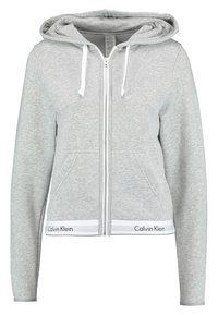 Hanorac cu fermoar gri, realizat dintr-un material moale, având glugă cu șnur, două buzunare frontale și o bandă albă cu logo-ul "Calvin Klein" la tiv.