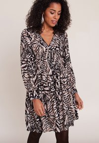 Robe à manches longues et longueur genoux dans un motif de feuilles noir, beige et blanc, avec un décolleté en V et un détail de taille froncée.