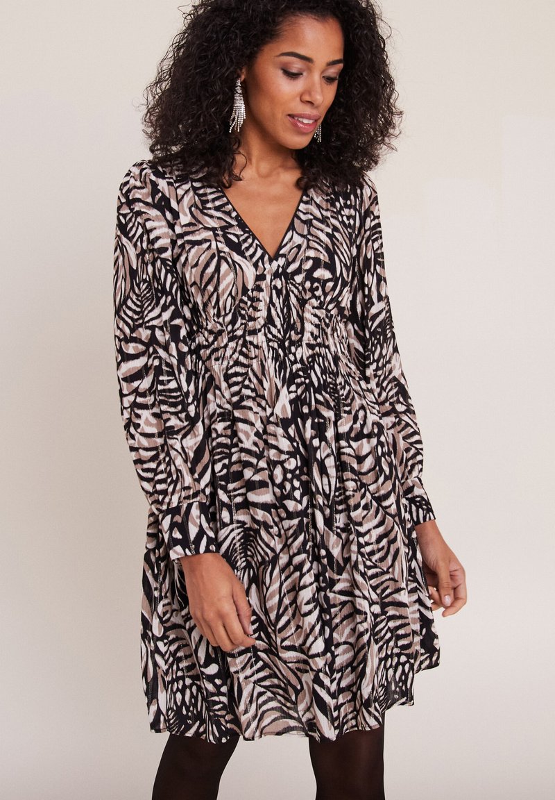 Robe à manches longues et longueur genoux dans un motif de feuilles noir, beige et blanc, avec un décolleté en V et un détail de taille froncée.