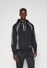 Sweatshirt preto com capuz, apresentando painéis laterais cinzentos e riscas brancas. A parte frontal exibe o logótipo. Feito de um tecido macio e texturizado com um corte descontraído.