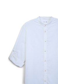 Camicia bianca con colletto rialzato, maniche lunghe arrotolate fino al gomito e piccoli bottoni lungo il davanti. Tessuto dalla texture liscia.