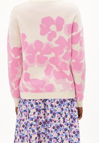 Stickad tröja i krämfärg med stora rosa blommönster, med ribbad nederkant och muddar. Bärs över en flerfärgad blommig klänning.