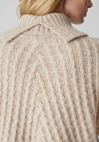 Strickpullover in hellbeige mit einem gerippten Kragen. Verfügt über ein strukturiertes Zickzackmuster und eine weiche, flauschige Textur.