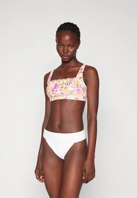 Haut de bikini floral aux nuances roses et jaunes, avec un décolleté carré et des bretelles larges ; associé à un bas de bikini blanc côtelé taille haute.