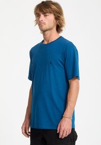 Blaues T-Shirt mit Rundhalsausschnitt aus weichem Stoff, mit kurzen Ärmeln und einem kleinen schwarzen Logo auf der Brust. Glatte Textur, lockerer Schnitt.
