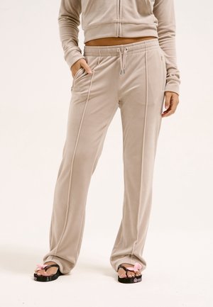 Beige bløde stofbukser med forstærkede syninger foran og snøre, båret sammen med sorte platformsandaler med pink sløjfer.