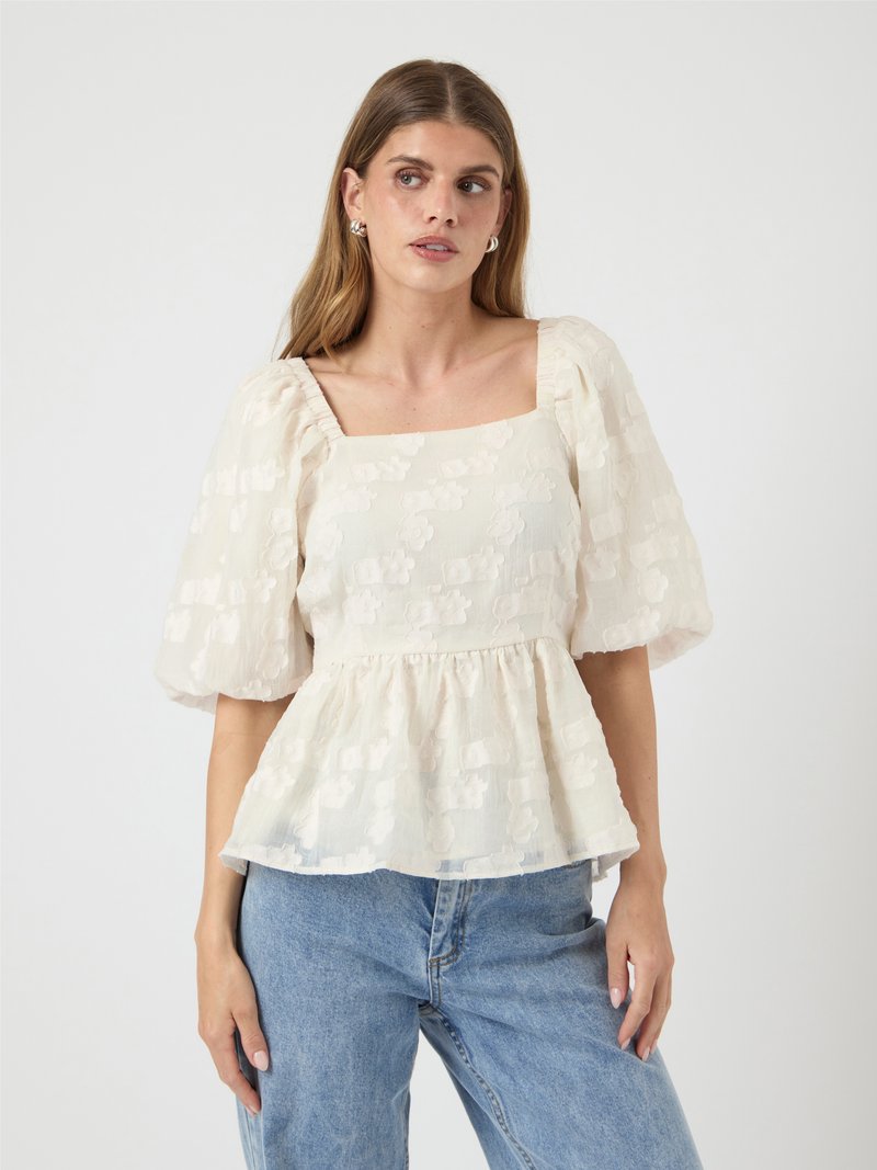 White peplum top with puff sleeves, featuring a square neckline and floral textured pattern. Paired with light blue high-waisted jeans.